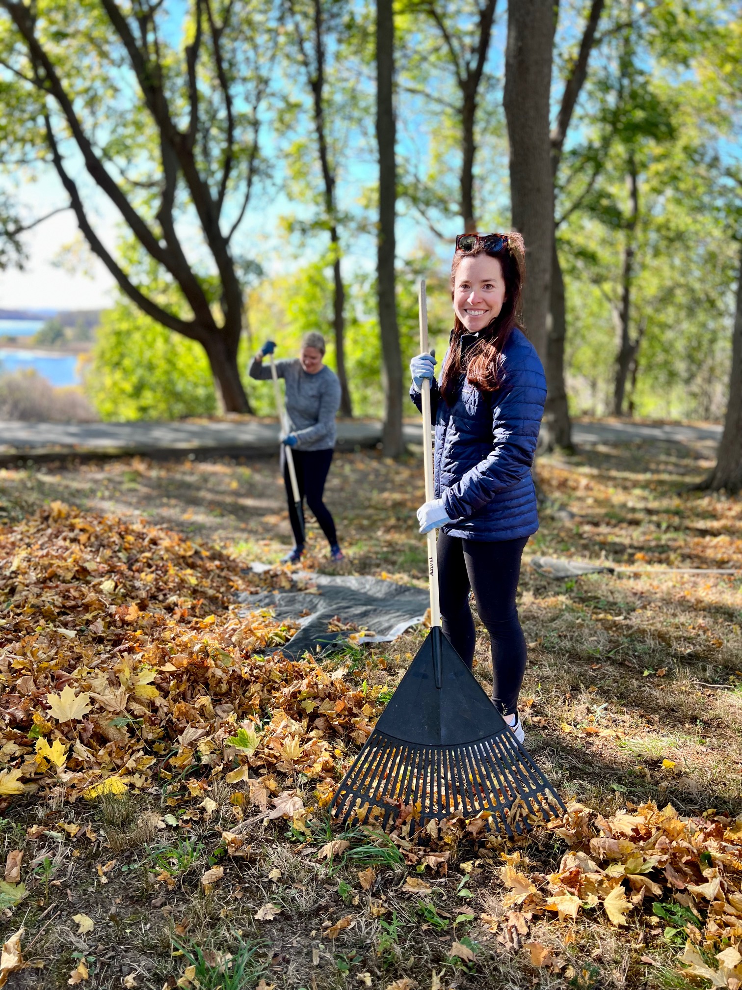 A team member pauses from raking leaves and smiles.