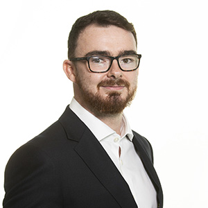 Professional man in business attire with glasses posing for a corporate headshot against a white background.