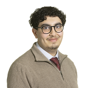Man with curly black hair and glass wearing a beige sweater
