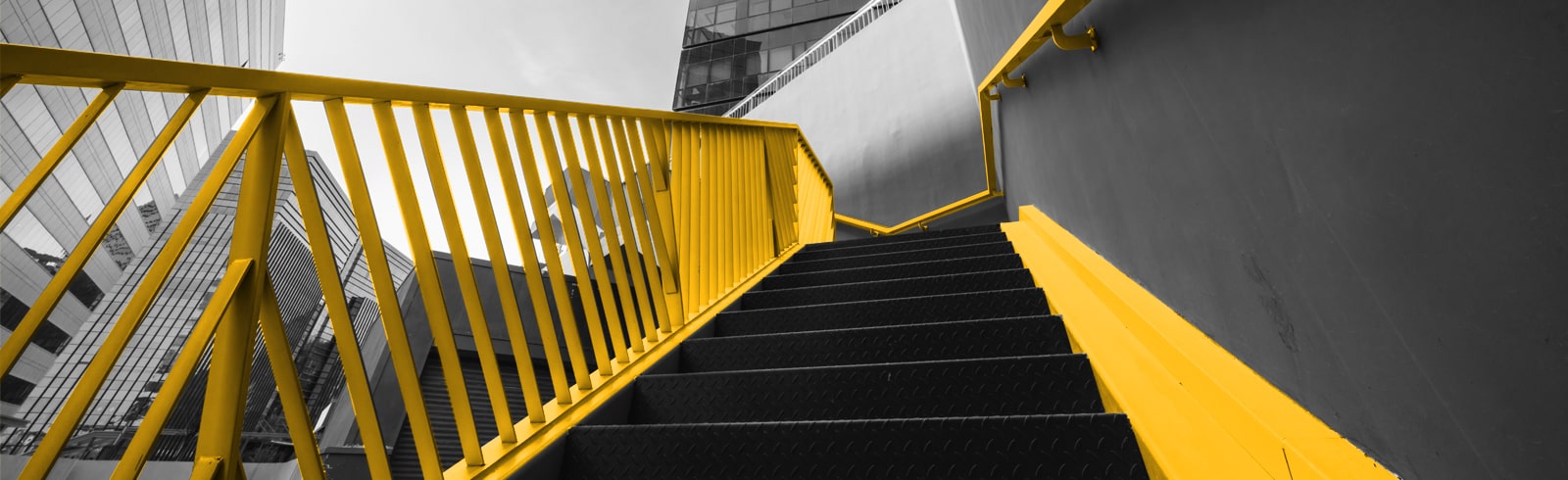 A vivid yellow staircase contrasting against a monochrome urban backdrop, indicating a selective colour technique in architectural photography with a focus on modern design and industrial aesthetics.