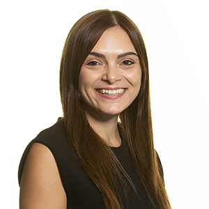 Professional woman with long brown hair smiling in business attire against a white background.