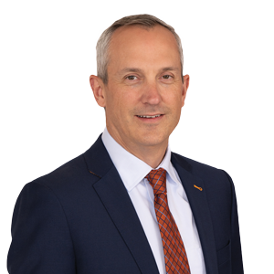 Professional middle-aged man in business attire with a friendly demeanour, wearing a navy blue suit, white shirt, and orange tie, against a white background.