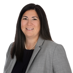 Professional woman with long hair wearing a business suit and pearl necklace smiling in a corporate headshot.