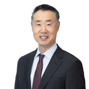 Professional middle-aged businessman smiling in a studio portrait, wearing a dark suit with a blue tie and white shirt, representing corporate leadership and confidence.