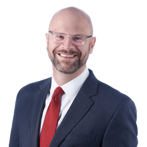Professional bald man with beard smiling, wearing spectacles, a dark suit and red tie against a white background.