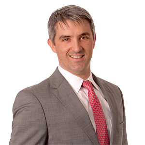 Smiling businessman in grey suit with pink tie against a white background with stripe pattern.