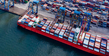 Aerial view of a cargo ship at a busy container port, illustrating international trade, maritime logistics, and global shipping operations.