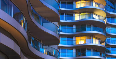 Modern architecture featuring curved balconies on a residential high-rise building during twilight with illuminated windows in urban cityscape