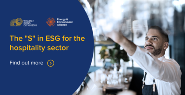 Professional bartender reaching for a glass in a sustainable hospitality environment, promoting the 'S' in ESG for the hospitality sector with Energy & Environment Alliance logo