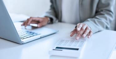 Professional working on laptop with calculator on desk in a modern office setting, highlighting financial analysis and business accounting.