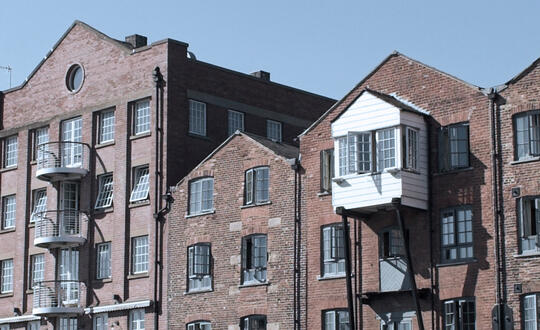 Traditional British red brick warehouse conversions with white-framed windows under clear blue sky, reflecting heritage and urban regeneration in the UK.