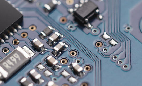 Close-up of electronic circuit board with microchips, capacitors, and detailed copper tracks and connections on a blue background.