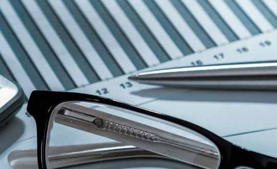 Pair of spectacles on financial documents with graphs, pen, and calculator in the background, indicating business analysis and strategic planning.