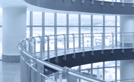 Modern glass balustrade on spiral staircase in contemporary office building interior, with panoramic windows and cityscape view, in monochrome blue tone.