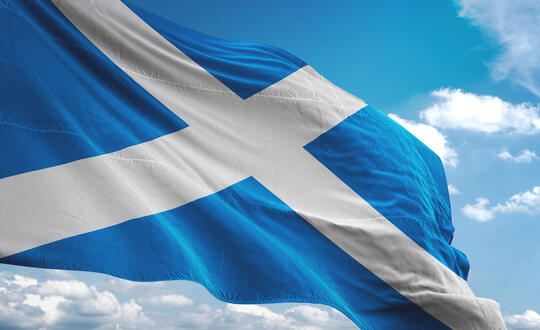 A vibrant Scottish Saltire, also known as the St Andrew's Cross, fluttering against a backdrop of a partly cloudy sky.