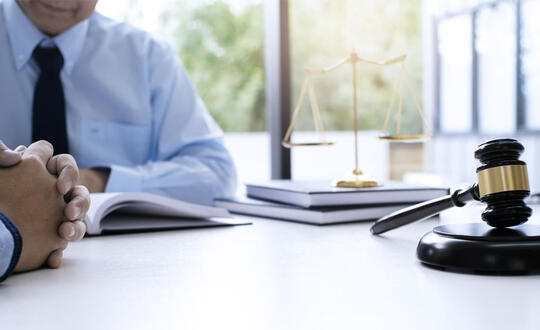 Lawyer taking notes while sitting at a table with client - Shutterstock 741939232