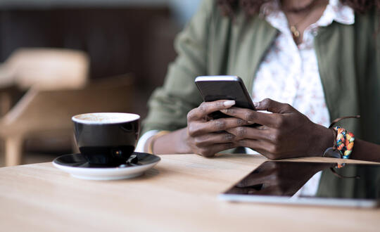 Woman holding cell phone at a table beside mug and tablet - Getty Images 921231310