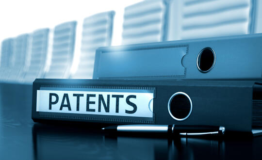 A binder labeled with "Patents" laying on a corporate meeting table - Shutterstock 504559510