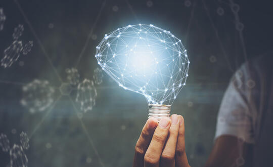 A man holds a lightbulb with a light in the shape of a brain attached - Shutterstock 1118418242