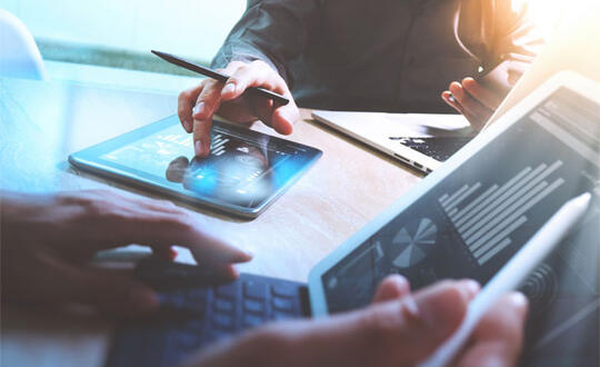 Two people look at financial graphs on a computer and tablet - Photo from Shutterstock (492340057)