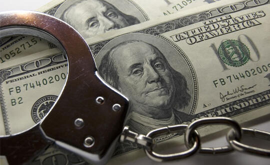 Handcuffs lay on top of two U.S. $100 bills - Photo from Shutterstock, ID 1766714
