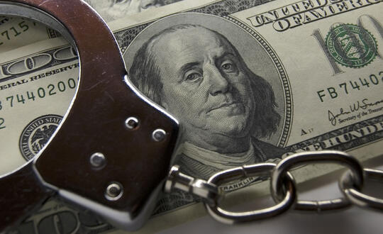 Handcuffs lay on top of two U.S. $100 bills - Photo from Shutterstock, ID 1766714