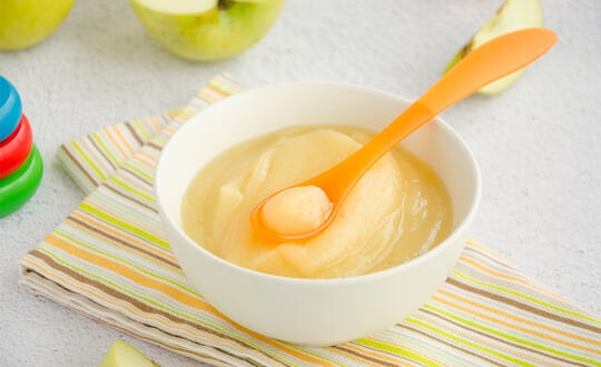 Apple sauce with a children's spoon surrounded by apples and toys