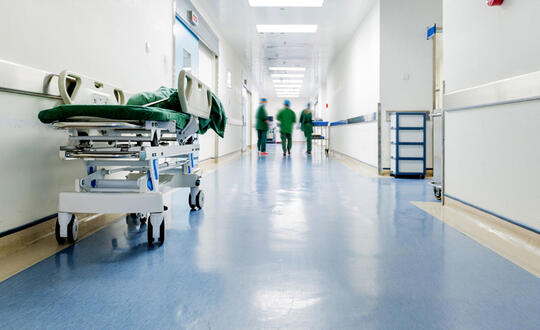 A gurney sits on the left side of a hospital hallway as three nurses walk further down