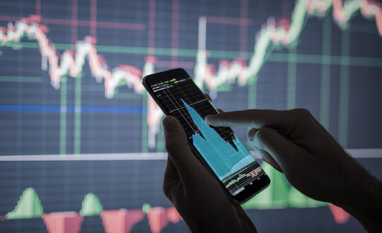 A person checking stock market data on a cell phone, with analysis economy data on forex earn graph.