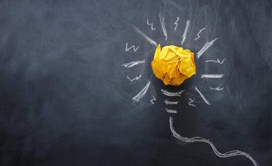 A crumpled, yellow paper symbolizes a light bulb on a chalk drawing of a glowing light