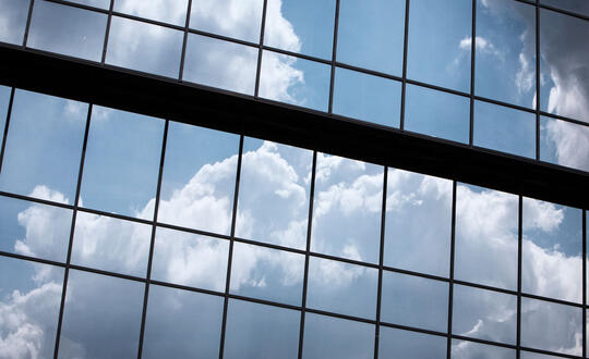 Reflection of cumulus clouds in the glass facade of a modern office building, showcasing a contrast between nature and urban architecture under a partly cloudy sky in the UK.