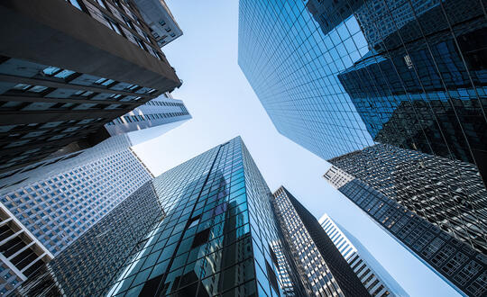 Looking up at a stunning cityscape of towering skyscrapers under a clear blue sky, showcasing modern architecture and urban development in a major city's financial district.
