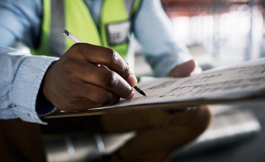 Close-up of architect's hands reviewing blueprints on a desk at a construction site.