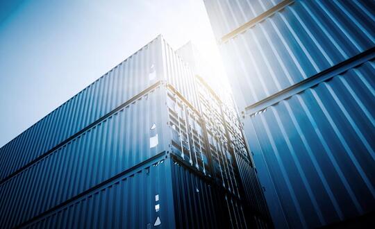 Low-angle view of modern skyscrapers with reflective glass facades under a clear blue sky, sun flare gleaming off buildings in a bustling metropolitan business district.