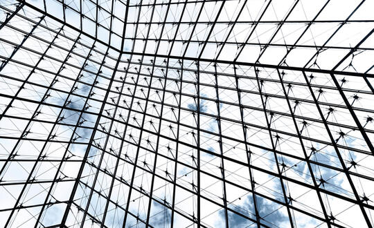 Glass ceiling with geometric steel framework against a blue sky with clouds, symbolising modern architecture and design.