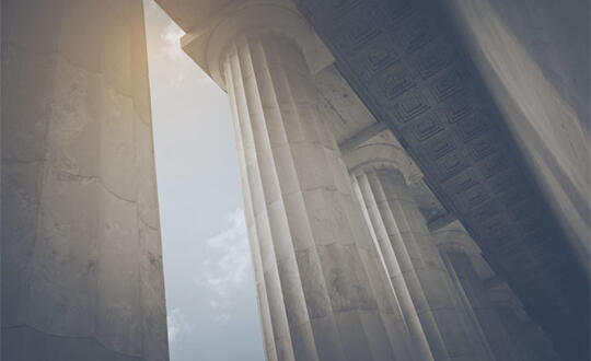 Pillars of a courthouse stand against the blue sky.
