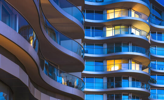 Modern architecture featuring curved balconies on a residential high-rise building during twilight with illuminated windows in urban cityscape