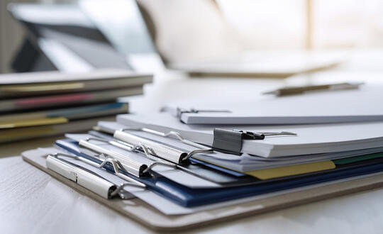 A stack of organised office paperwork and folders with pens on a white desk, signifying efficient workplace administration and document management.