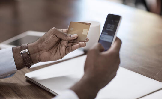 Person holding a credit card and a smartphone to perform a contactless payment, symbolising secure mobile banking and convenient financial transactions.