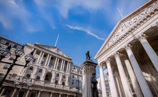 The iconic Royal Exchange building beside the Bank of England with a statue in the foreground, under a clear blue sky in the City of London, capturing the historic financial district's architecture.