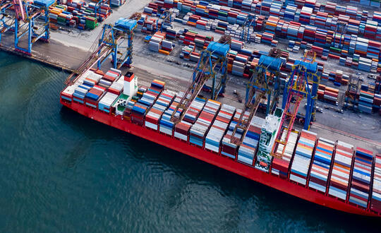 Aerial view of a cargo ship at a busy container port, illustrating international trade, maritime logistics, and global shipping operations.