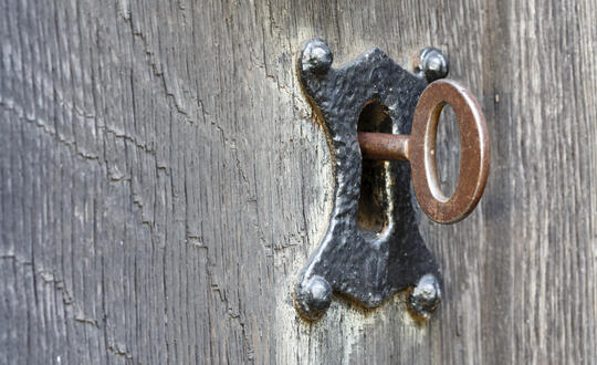 Rustic key in an old-fashioned keyhole on a weathered wooden door, illustrating vintage security and antique lock mechanisms.