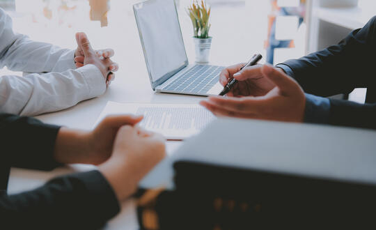Professional business meeting in progress with individuals discussing over a laptop, highlighting teamwork, corporate strategy, and collaborative office environment in a modern workspace.