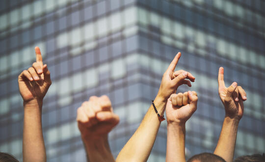 Photo of pointed hands in front of a corporate building block
