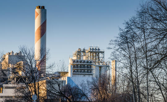 Industrial plant at sunrise with large chimney, pollution control systems, and clear blue sky.