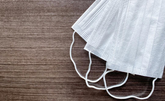 Two disposable medical face masks on a wooden surface, symbolising health safety and personal protective equipment during a pandemic.