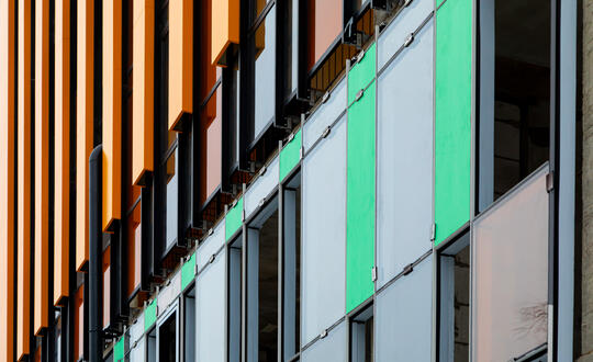 Modern urban architecture with contrasting coloured vertical fins and glass balcony panels at dusk.