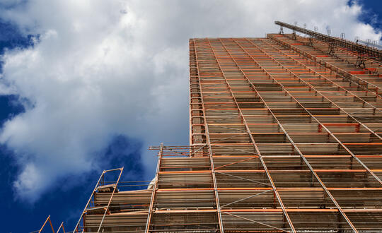 Construction scaffolding against a cloudy sky, illustrating building development and architectural framework in urban construction site