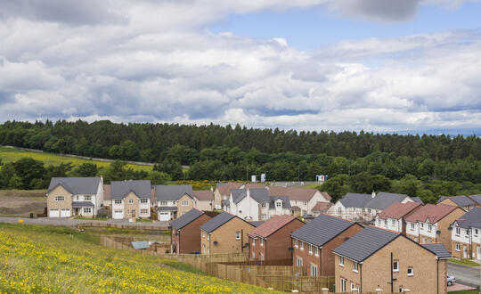 British housing estate with new-build homes set against a backdrop of green hills and cloudy skies, depicting suburban development in the UK.