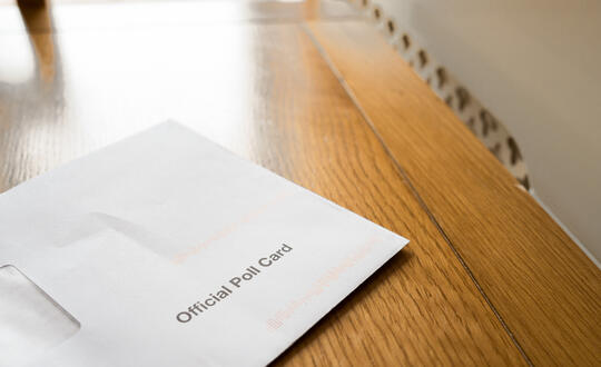 Shallow focus of a 2024 UK General Election Official Poll Card and envelope seen on a voters kitchen table.